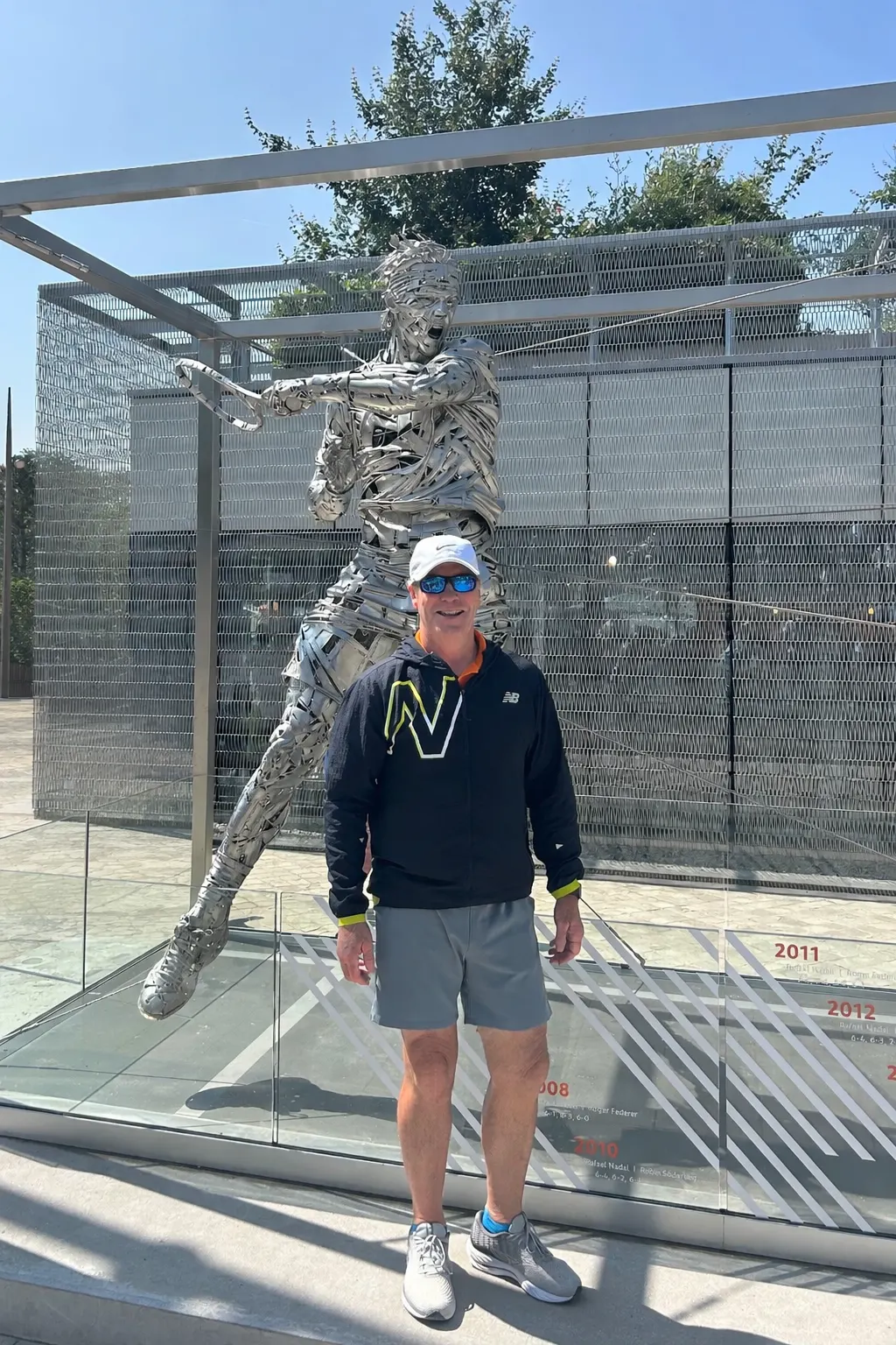 Coach Mike Moriarty next to a metal tennis champion sculpture during a destination tournament trip